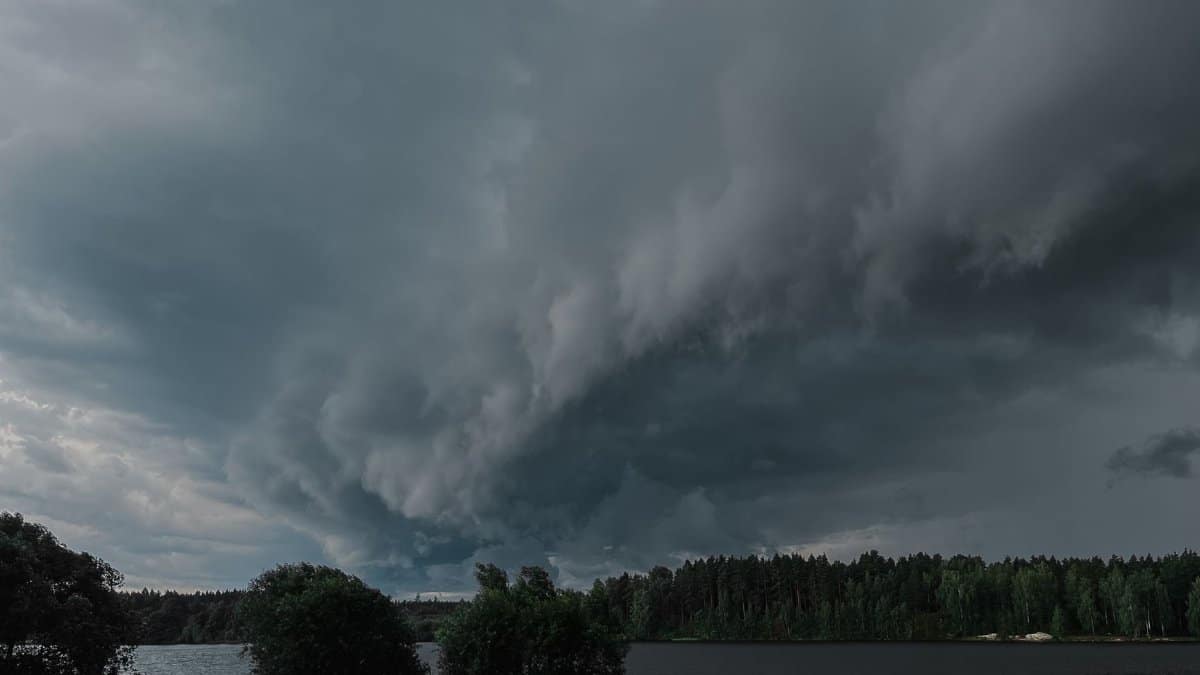 Dark storm clouds gather over a tranquil countryside lake, creating a dramatic and atmospheric scene.