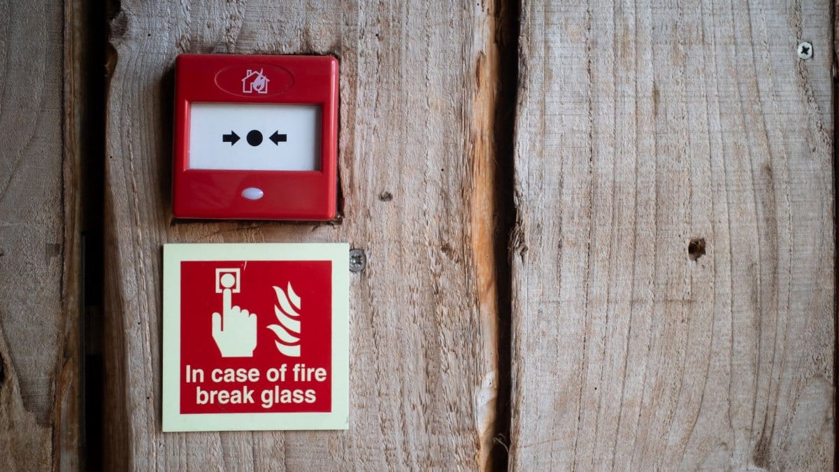 Red fire alarm and warning sign on a rustic wooden wall for safety awareness indoors.