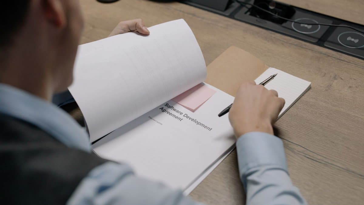 Business professional at the desk examining a software development agreement document.