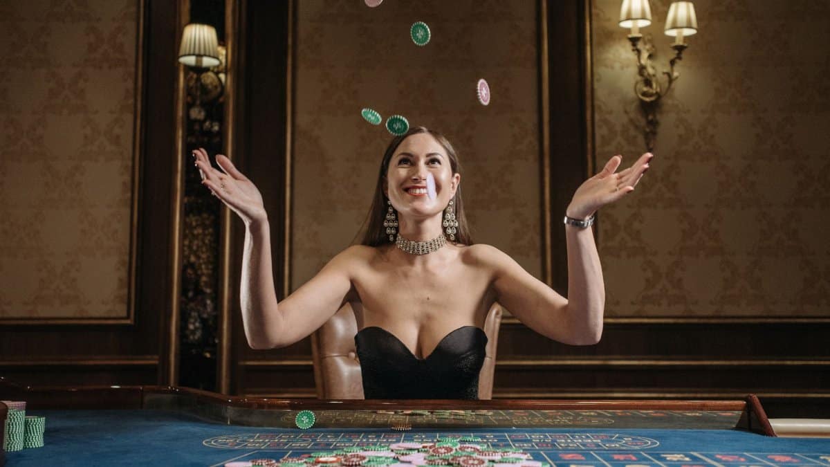 A smiling woman tosses casino chips up in an elegant gaming room, exuding joy.