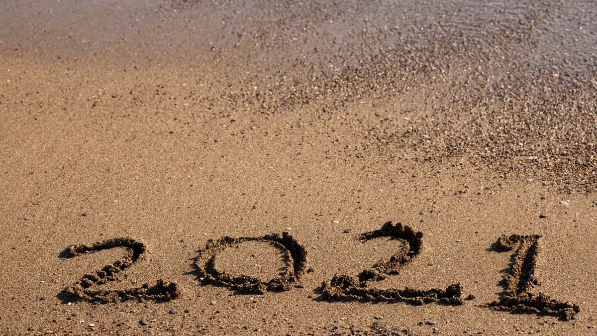 2021 written on the beach sand with ocean waves approaching.
