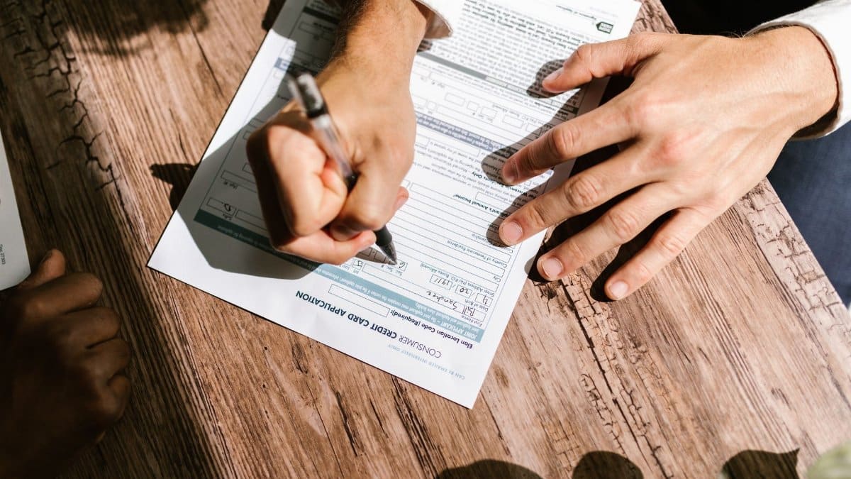 Hands writing on a consumer loan credit application form on a wooden table.