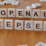 Close-up of wooden Scrabble tiles spelling OpenAI and DeepSeek on wooden table.