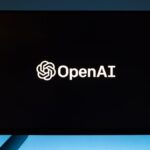 Minimalist display of OpenAI logo on a screen, set against a gradient blue background.