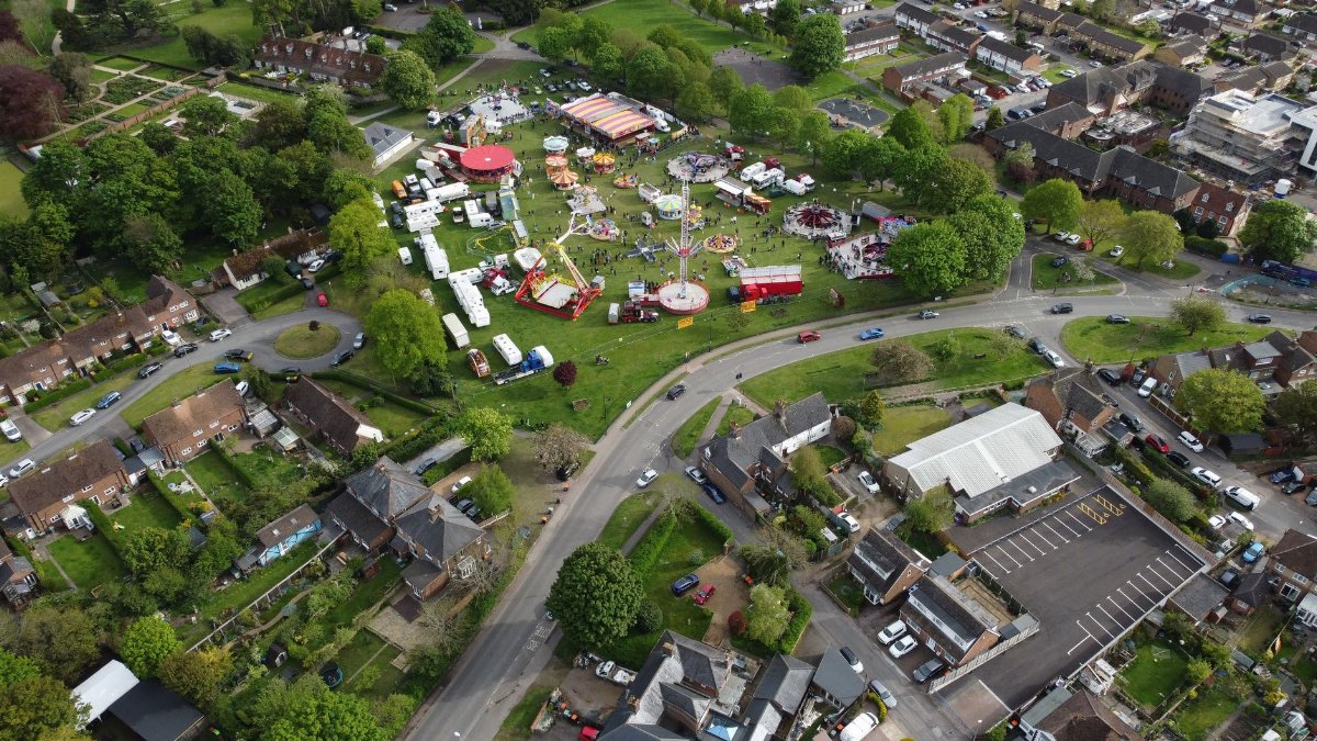 Aerial shot of a colorful funfair amidst green fields in Houghton Regis.