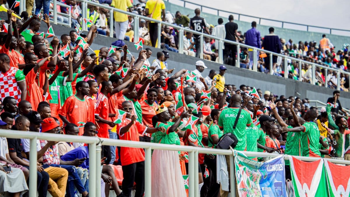 A lively crowd of fans cheering at a football stadium wearing team colors holding flags.