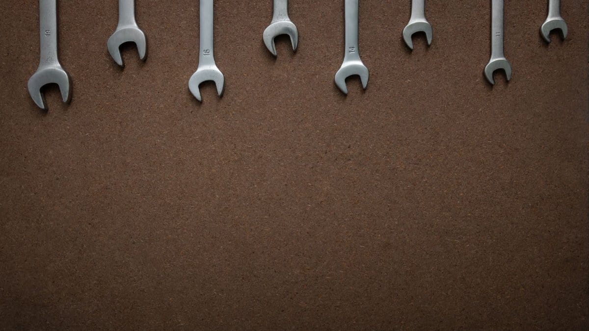 Flat lay of several wrenches lined up on a brown textured background with copy space.