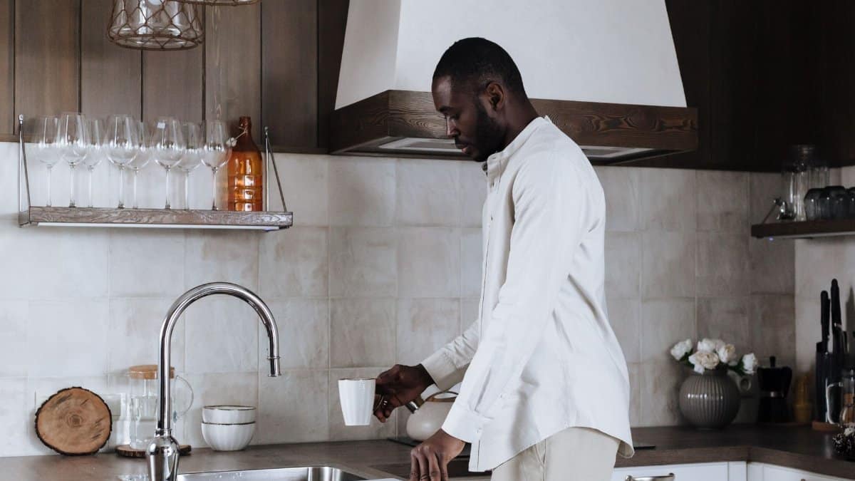 A man stands at the kitchen sink preparing a coffee cup in a modern home interior.