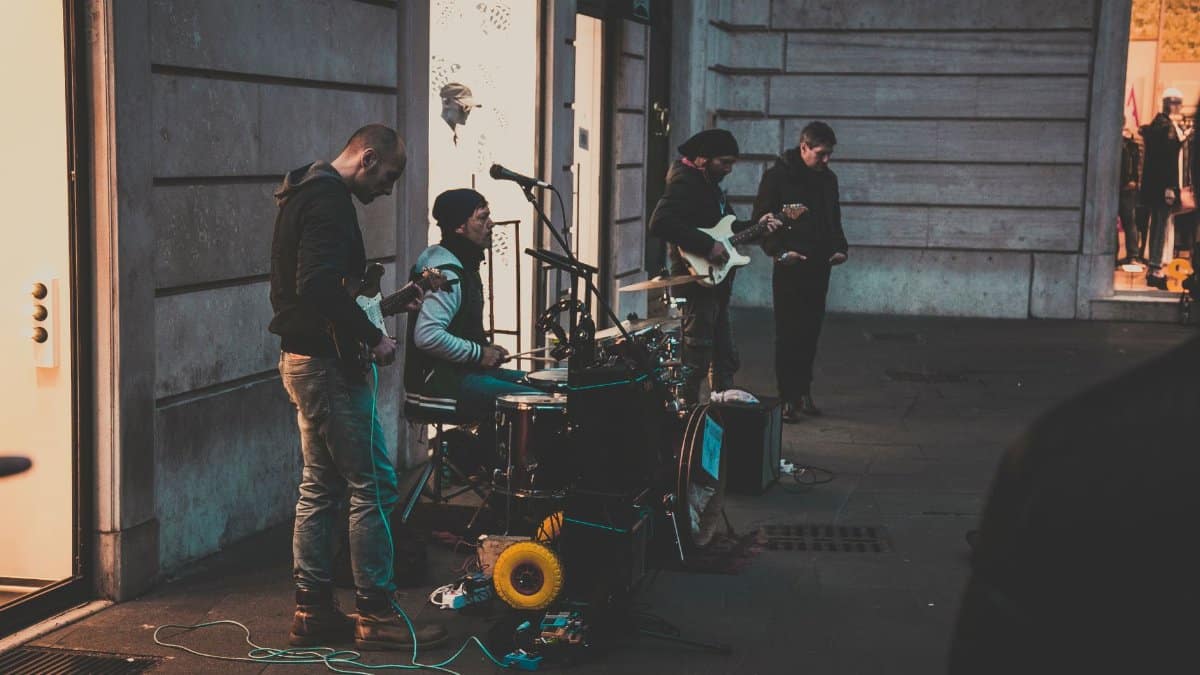 A group of street musicians performing with instruments on a city sidewalk during the evening.