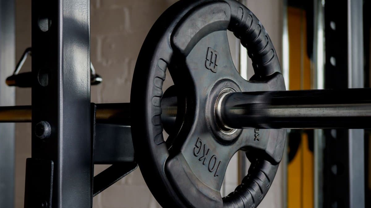 Close-up image of a barbell with a 10kg weight plate in a gym setting, emphasizing strength training equipment.