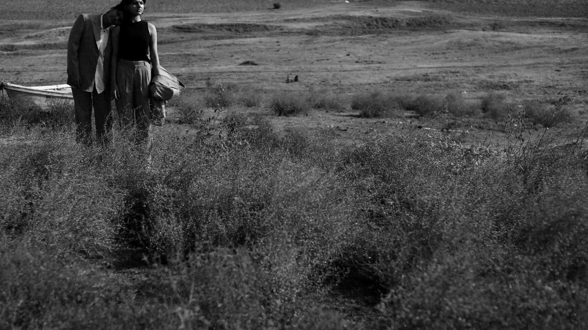 A couple shares a tender moment in a vast desert landscape in black and white.