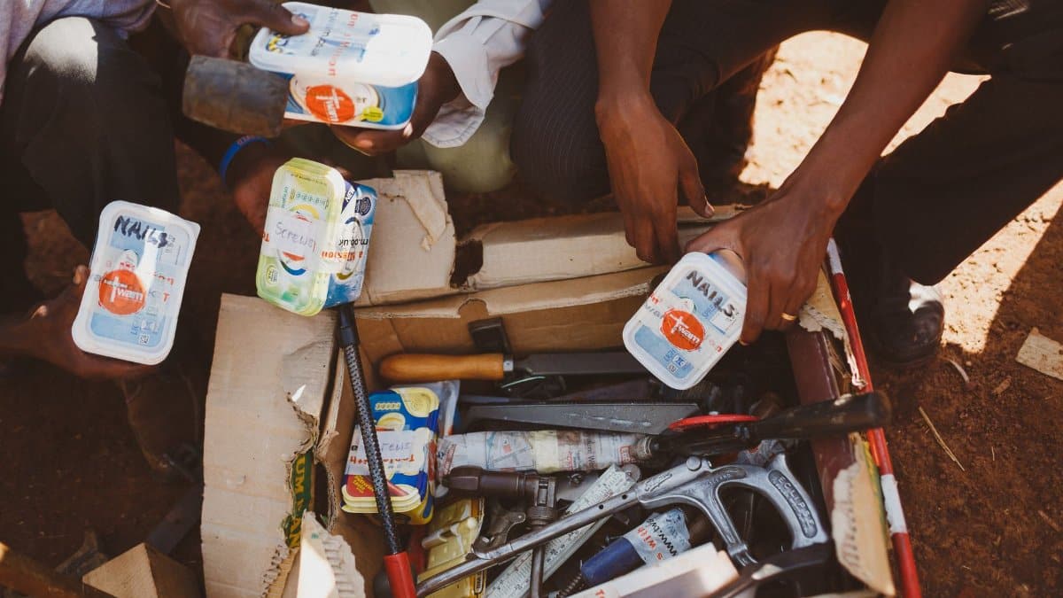 People sorting tools in a cardboard box outdoors in Wakiso, Uganda.