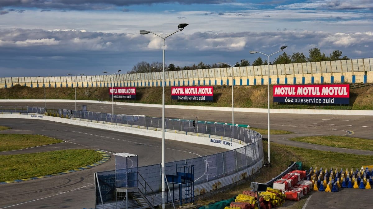 An empty motor racing track with advertising signs under a cloudy sky.