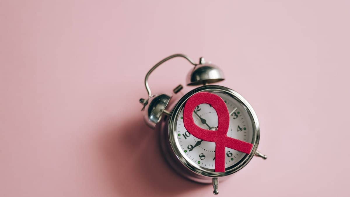 A still life of a pink ribbon on an alarm clock symbolizing breast cancer awareness.