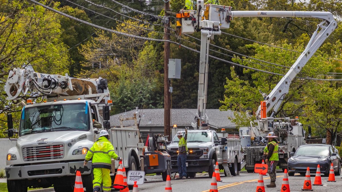 Utility workers in reflective gear repair power lines using bucket trucks and cones on a suburban street.