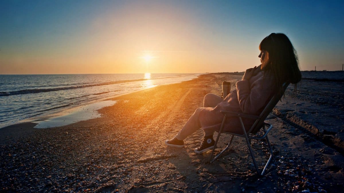 A woman sitting on a beach chair enjoying a serene sunset by the sea.