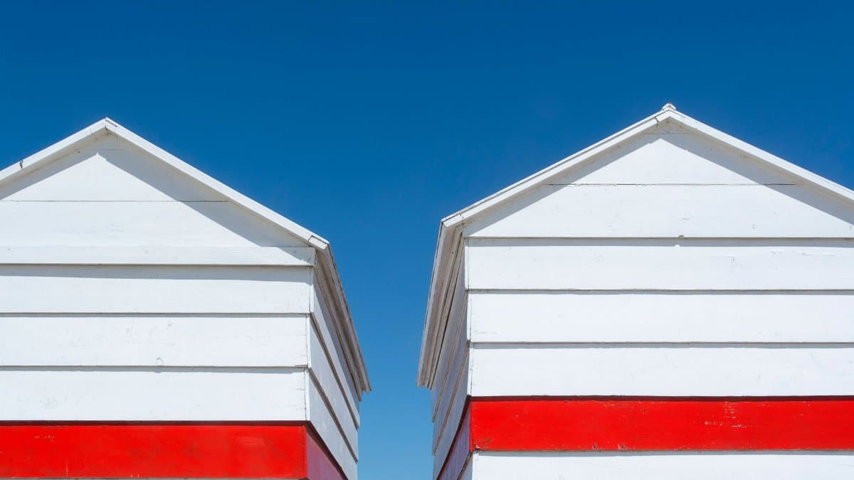 Two white and red beach huts with a clear blue sky background, captured in a low-angle shot.