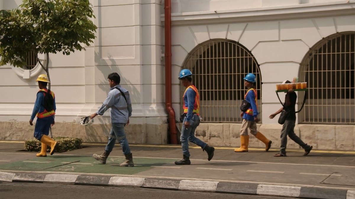 Group of construction workers walking along a city street under clear daylight conditions.