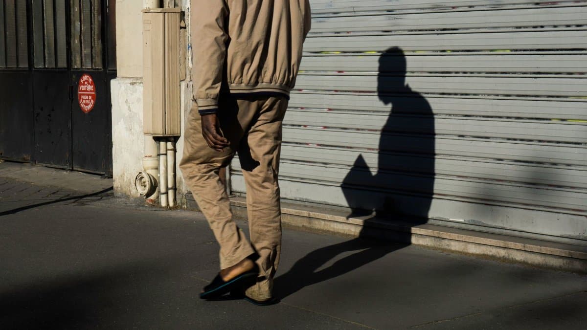 A person walks past a closed garage, casting a long shadow on the urban street.