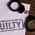 Top view of handcuffs on paper with 'GUILTY' text, symbolizing a verdict or crime.