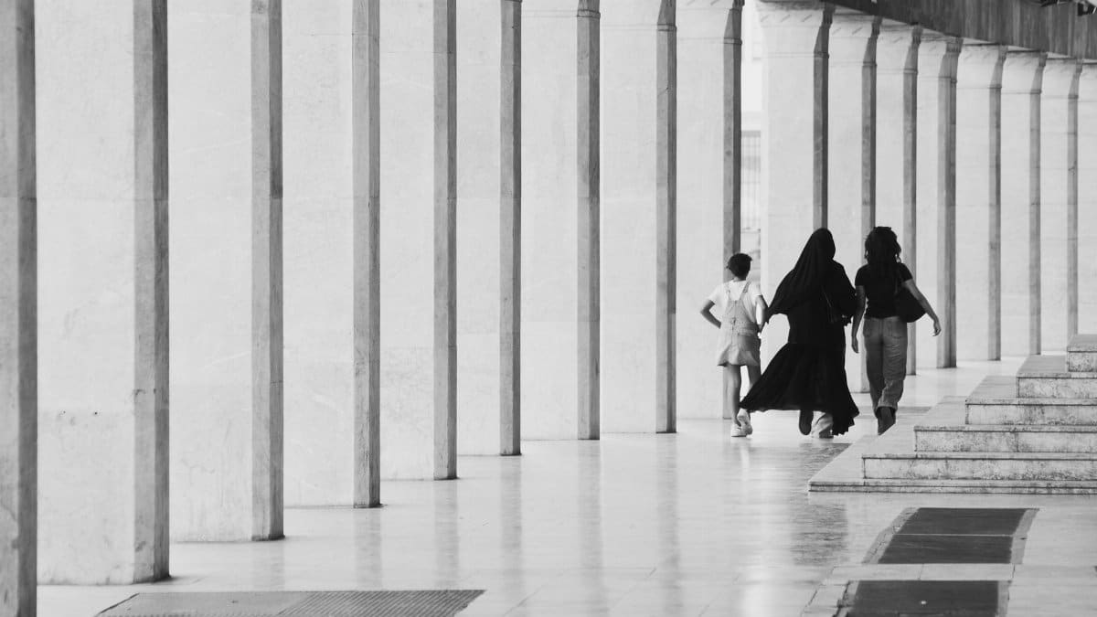 Black and white photo of three people walking through a corridor with columns in Rabat, Morocco.