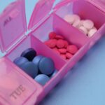Pink pill organizer with colorful tablets arranged for weekly medication management.