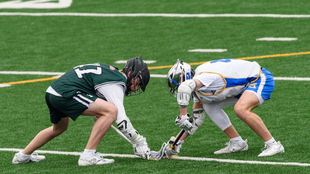 Two lacrosse players face-off on a vibrant green field, showcasing the sport's intensity and skill.