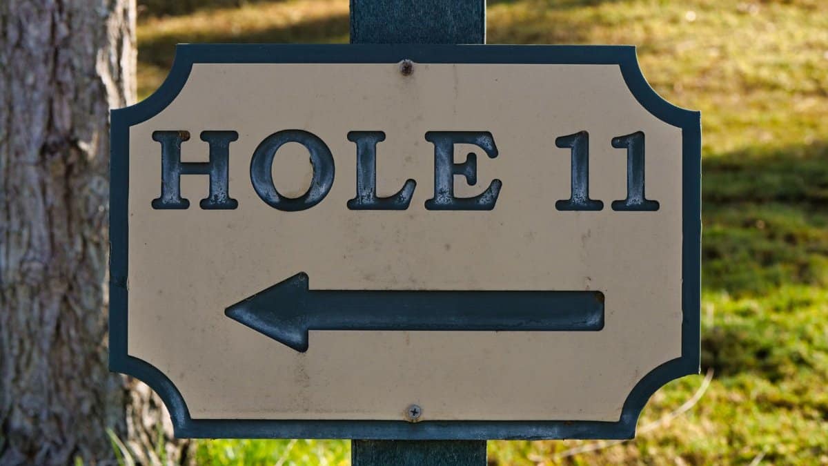 Close-up of a directional sign for Hole 11 on a golf course in daylight.
