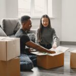 Happy couple unpacking moving boxes in their new apartment living room.