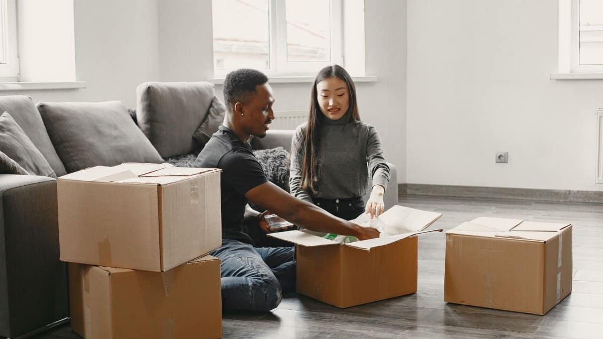 Happy couple unpacking moving boxes in their new apartment living room.
