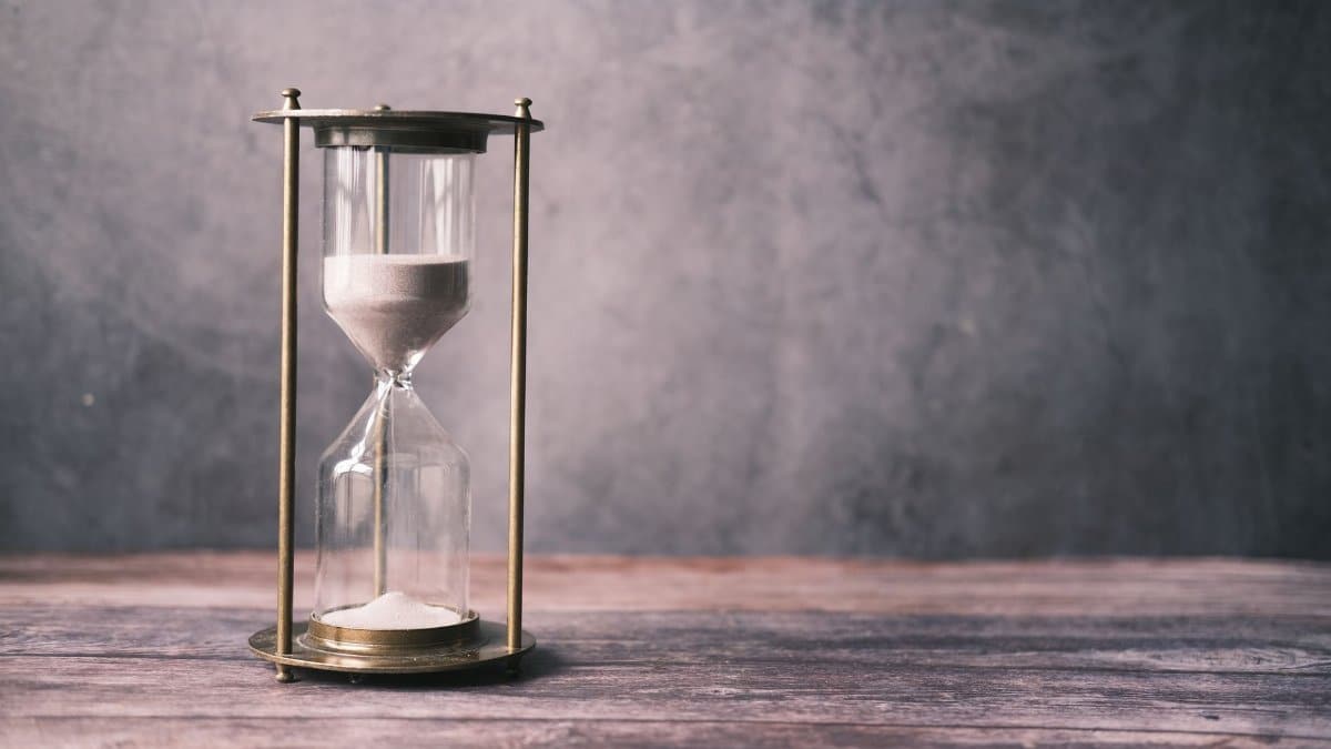 A classic hourglass with sand on a rustic wooden table against a soft gray background, offering ample copy space.
