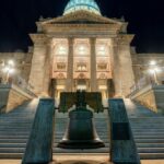Night view of a grand government building with a bell in the foreground, showcasing architectural symmetry.