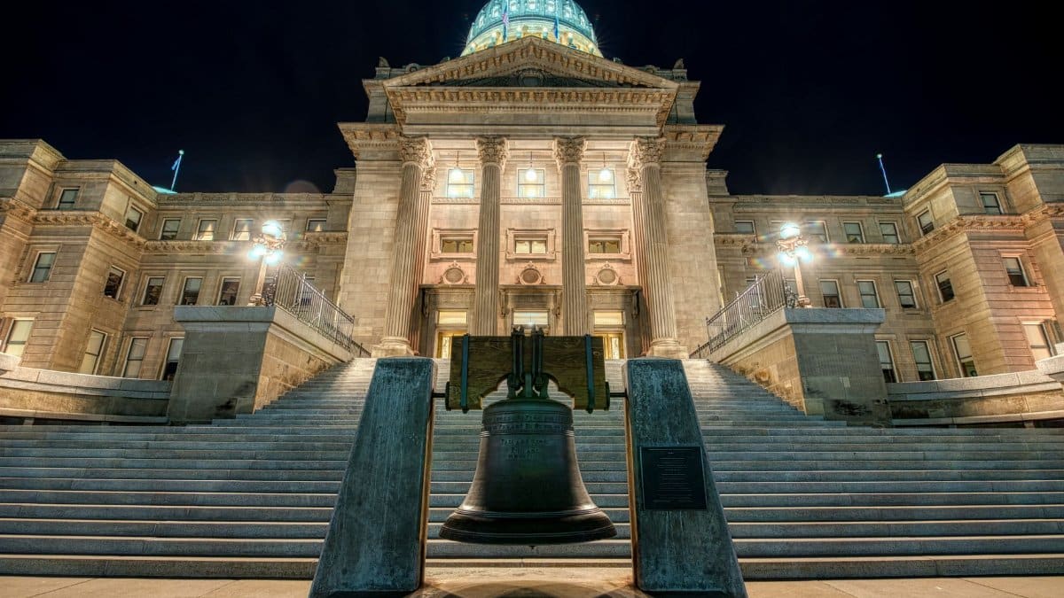 Night view of a grand government building with a bell in the foreground, showcasing architectural symmetry.