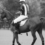 Polo umpire in action on horseback during a match, captured in black and white.