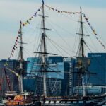 Historic USS Constitution sailing through Boston Harbor with city skyline in the background.