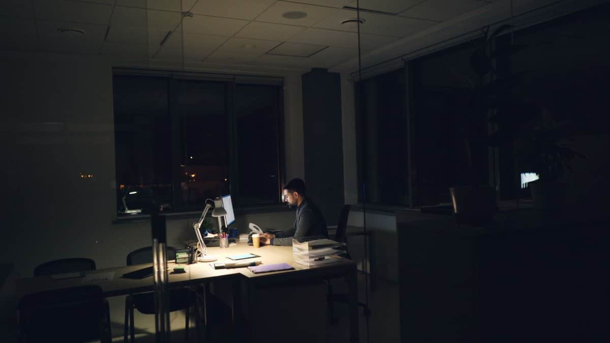 A man working late at night in an office, illuminated by desk light.