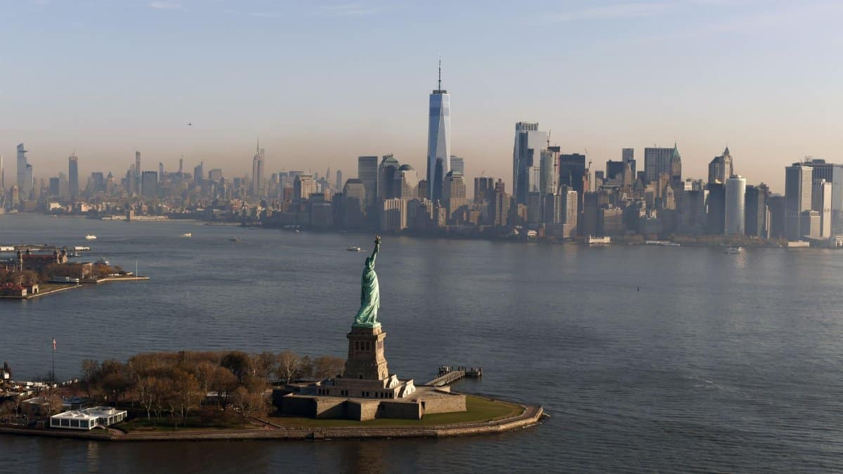 An aerial view of the iconic Statue of Liberty with New York City's skyline in the background.