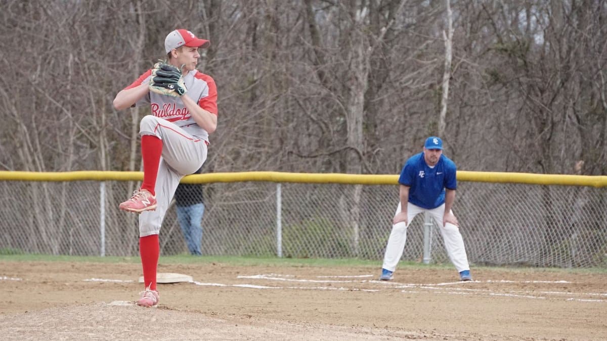 A high school baseball pitcher delivering a pitch during a game outdoors.