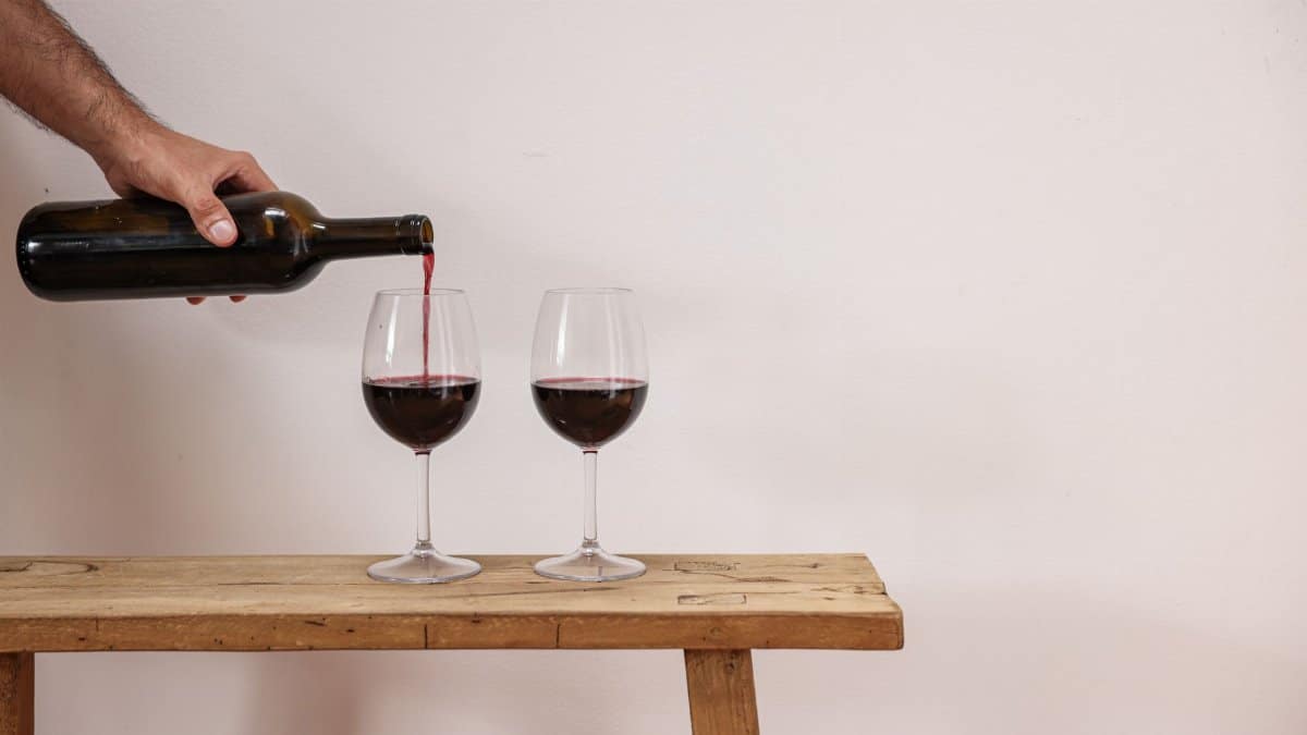 A person pours red wine into glasses on a rustic wooden table, elegant and simple.