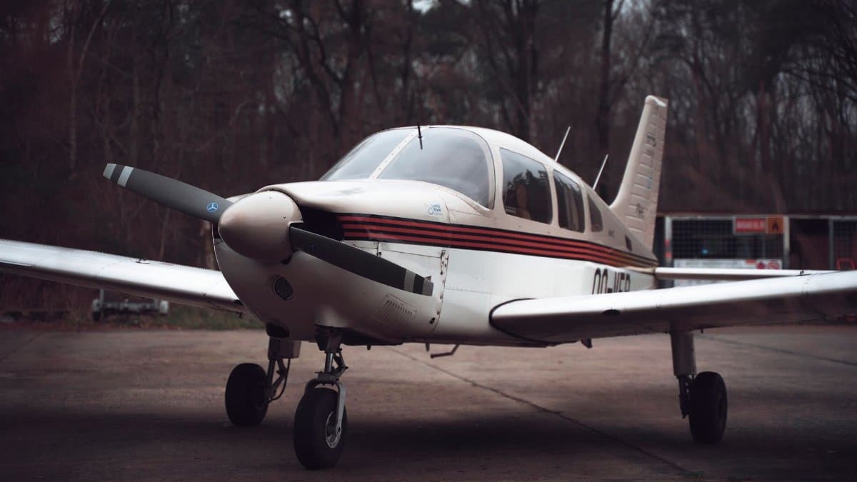A detailed view of a single-engine small aircraft parked on a runway surrounded by trees.