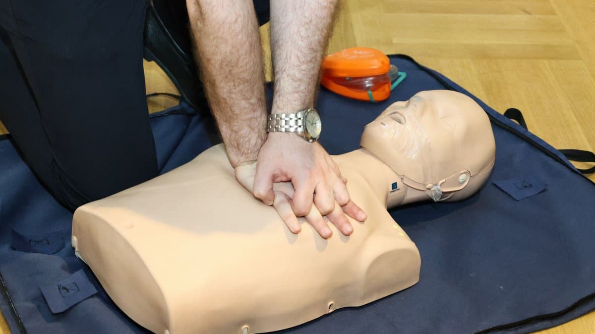 Hands performing CPR on a training dummy using realistic techniques indoors.