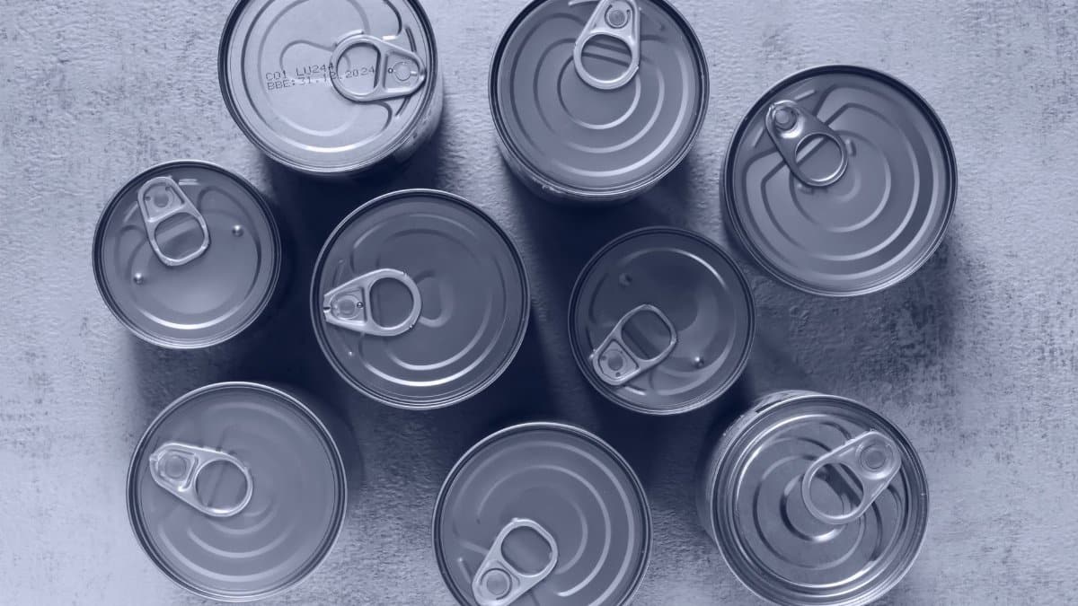 High-angle shot of canned food tins arranged on a rough surface, emphasizing texture and symmetry.