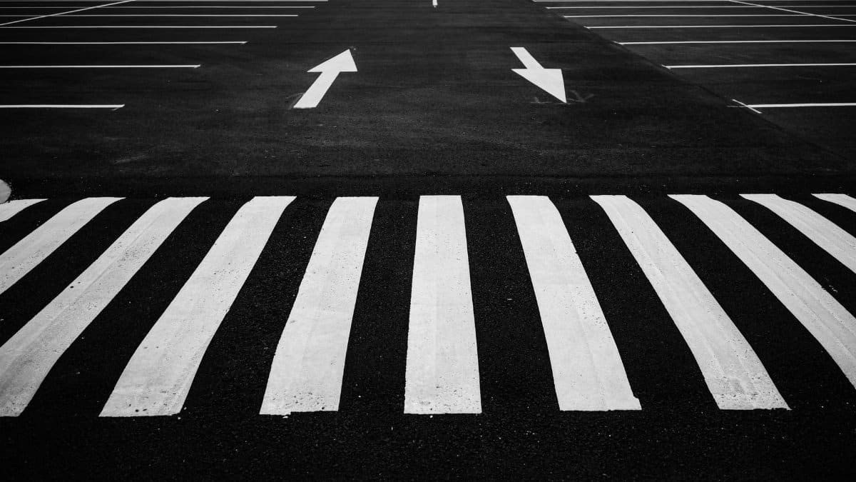 Black and white image of a parking lot with zebra crossing and directional arrows.