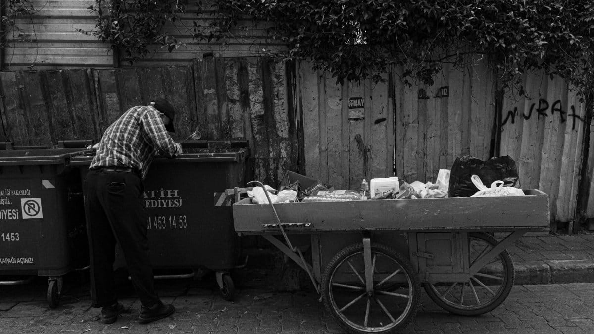 A poignant black and white street photograph depicting a man searching through trash in Istanbul, Türkiye.