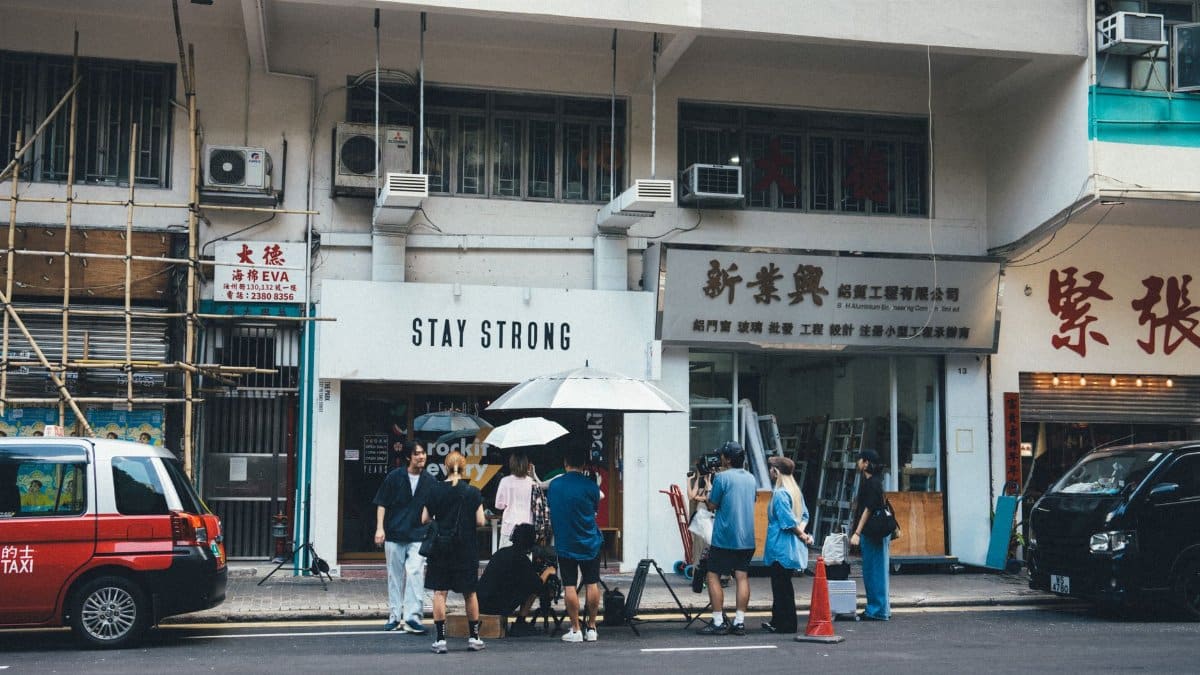 Group of people gather outside the Stay Strong store on a busy city street in daylight.