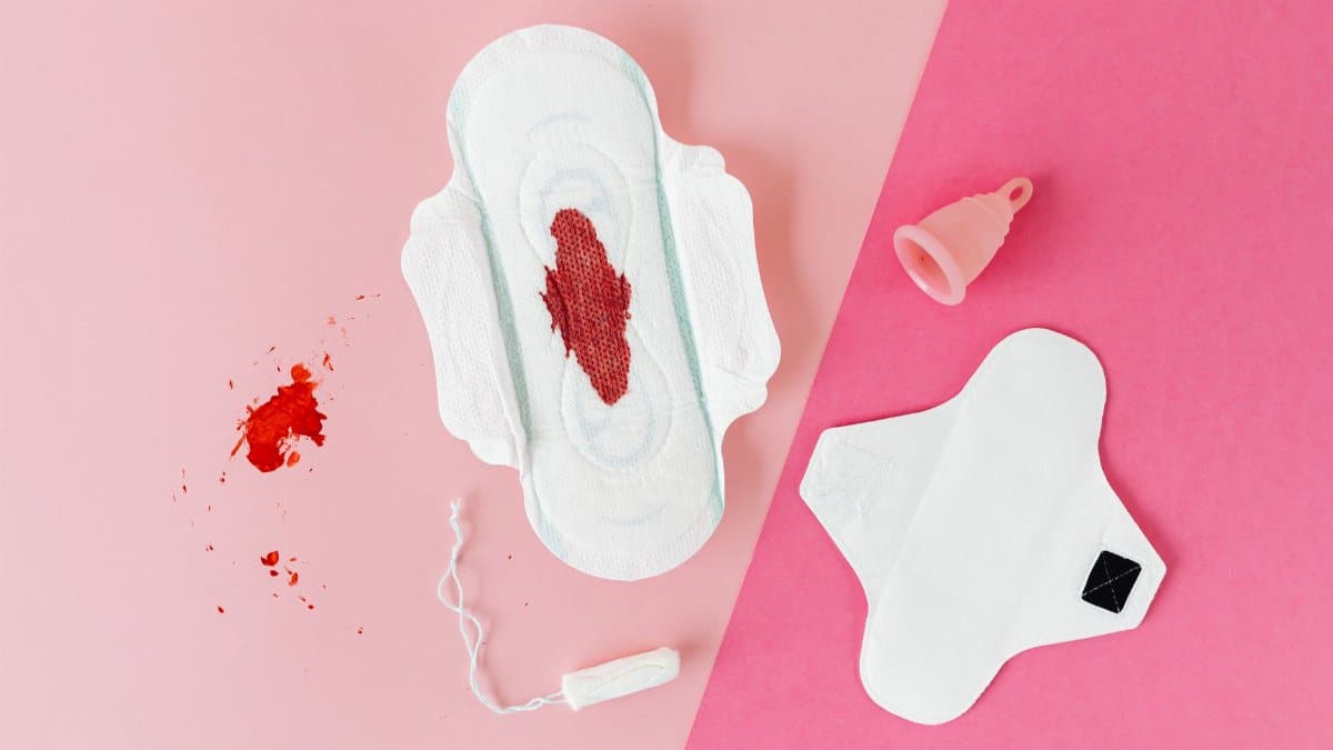 Flat lay of menstrual pad, cup, and tampon against a pink backdrop, highlighting period awareness.