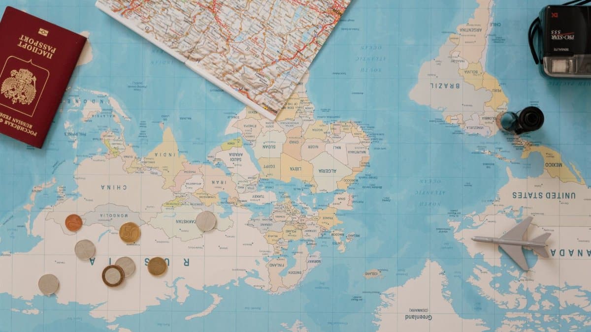 Flat lay of a world map, passport, coins, and camera for travel planning.