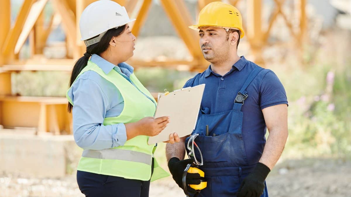 Male and female construction workers talking with safety gear at an outdoor site.
