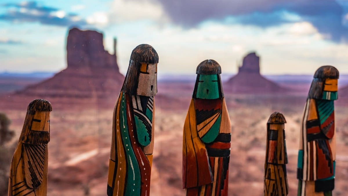 Colorful wooden totems with Monument Valley in the background during daylight.