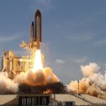 A NASA space shuttle launches with fiery liftoff, ascending into the sky amid plumes of smoke.